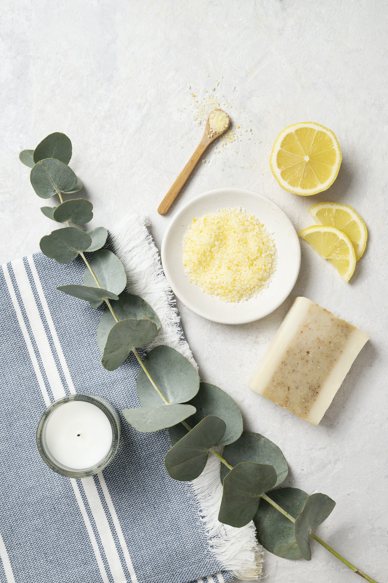 Organic yellow sea salt with lemon, soap and eucalyptus branch on a white textured background